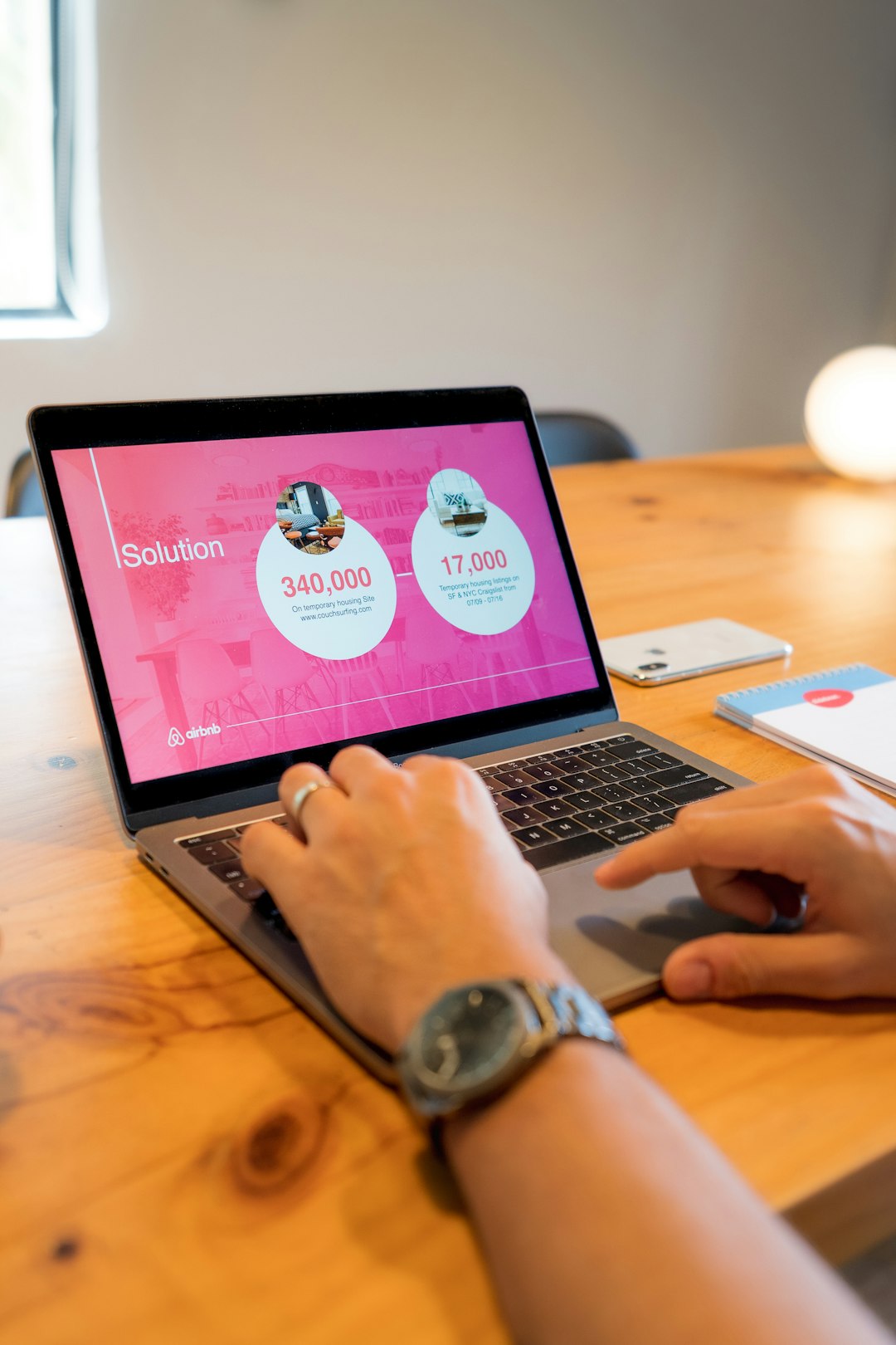 A startup founder working on his investor pitch deck. The laptop shows the Solution slide of the presentation, and the environment is a business office. Theres an iPhone cell phone in the background. The person is working at a wooden table.